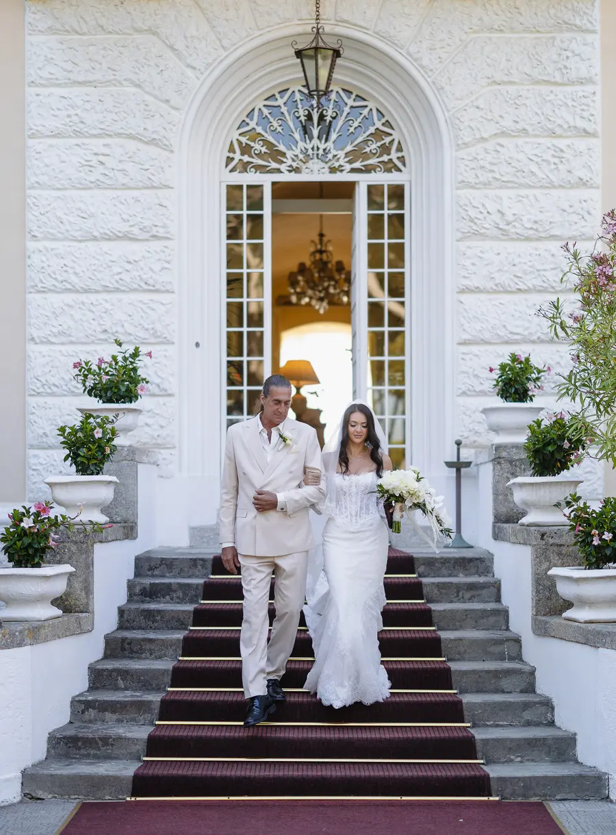 Bride walking down the Villa Parisi staircase on her father's arm along the red carpet