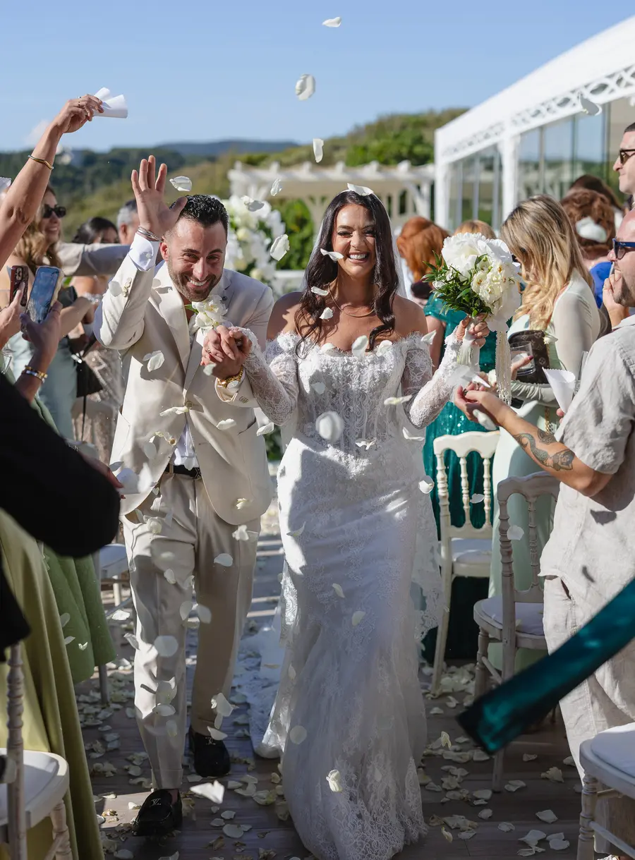 Smiling newlyweds leaving the ceremony as guests throw petals