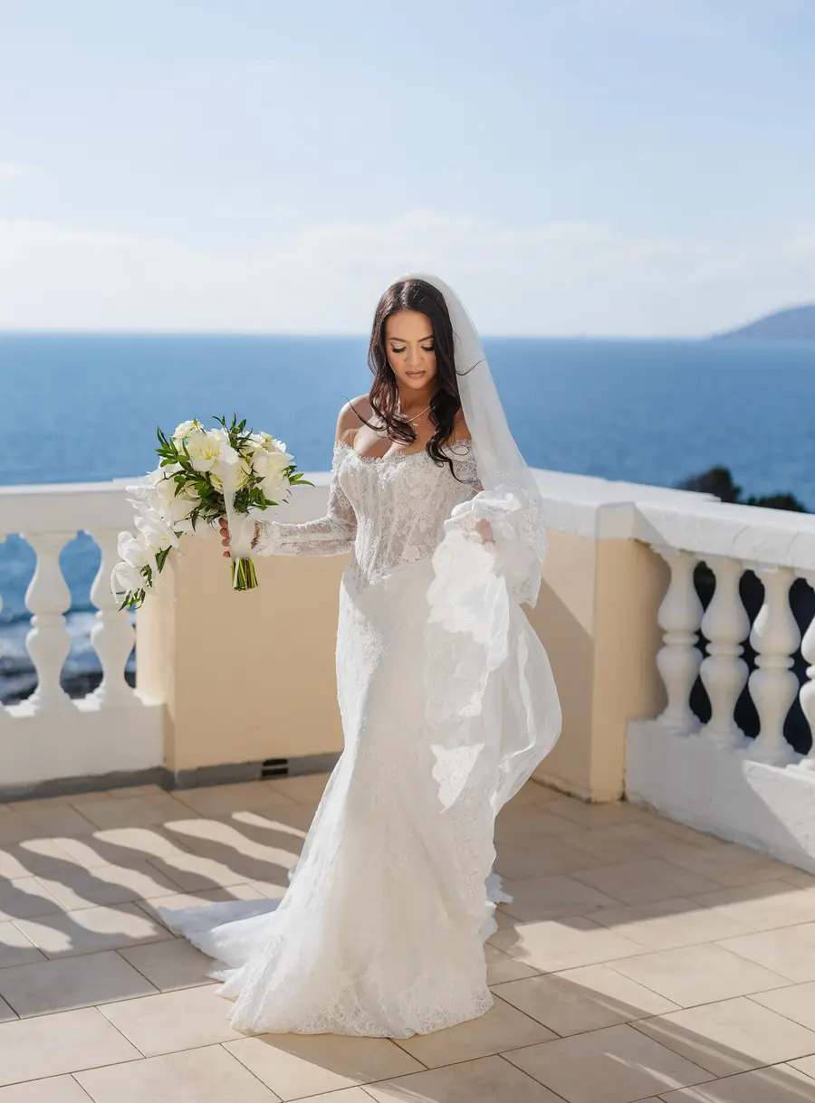 Bride in a lace wedding dress with bouquet walking on the terrace above the sea