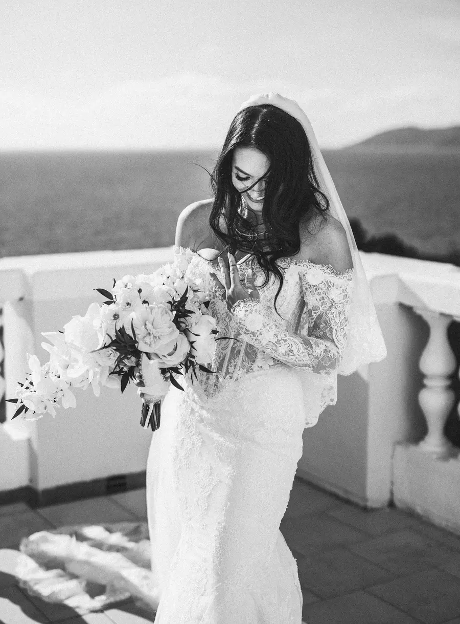 Black and white portrait of the bride smiling at her bouquet by the sea