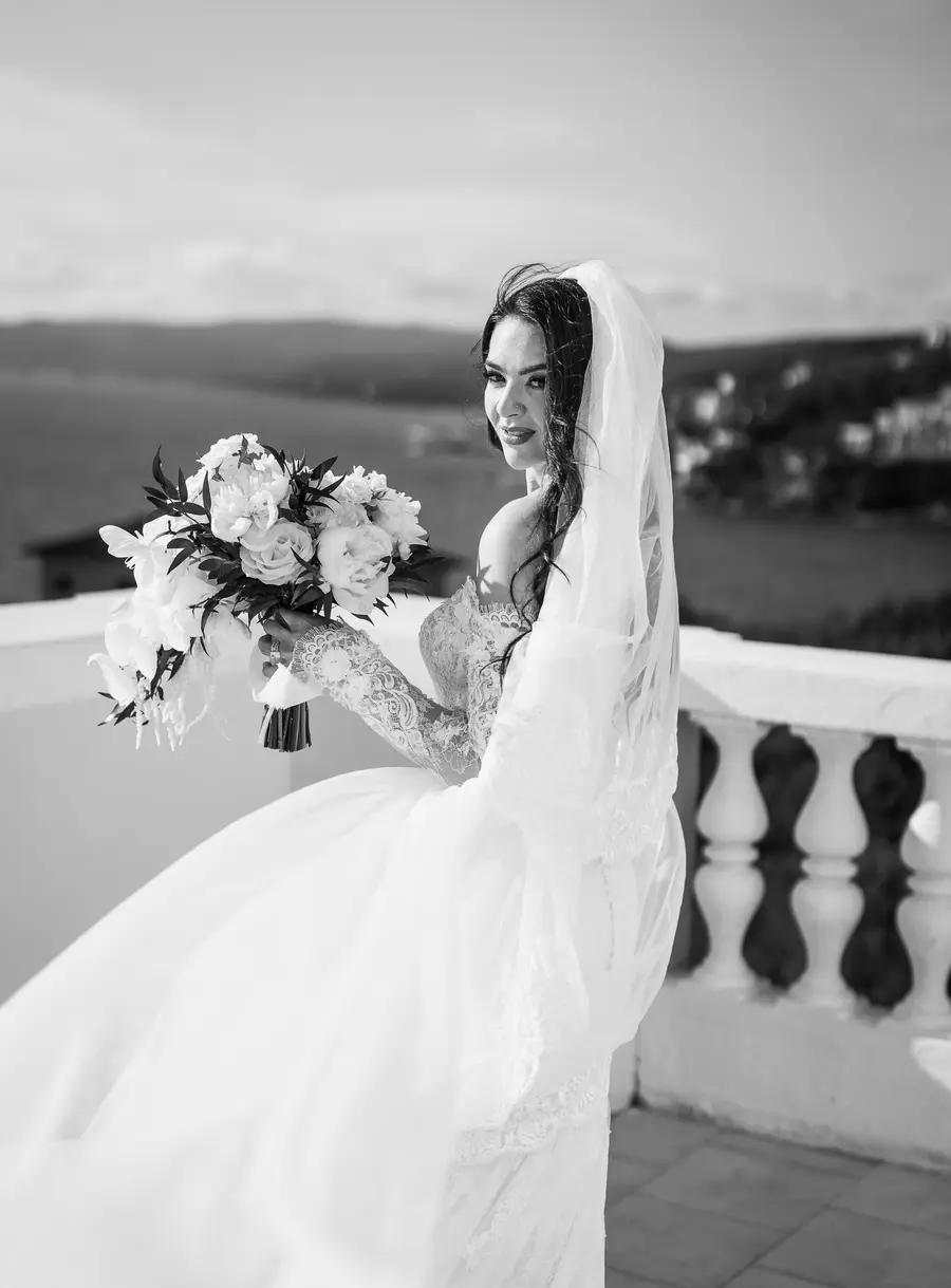 Bride with wind-blown veil and bouquet by the balustrade, black and white portrait