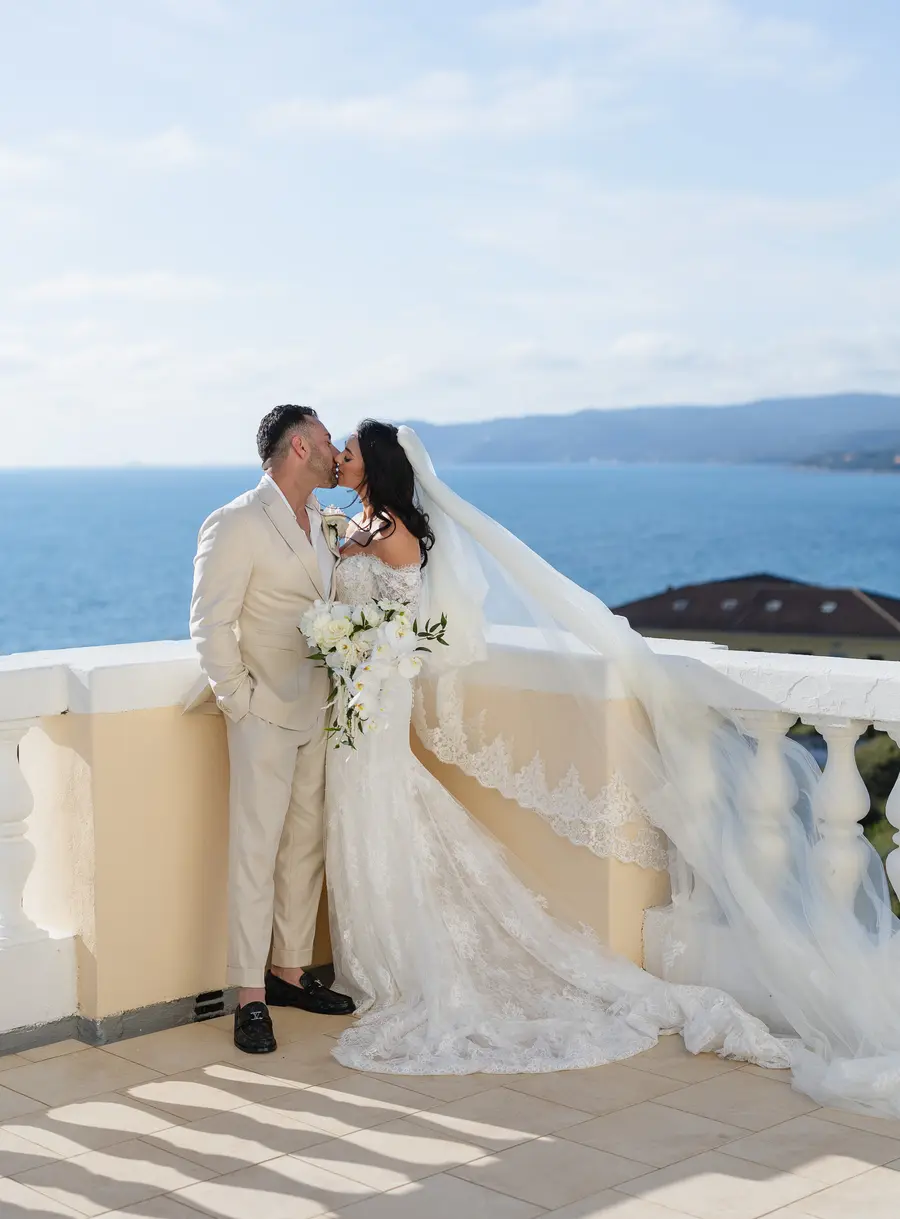 Couple kissing on the Villa Parisi terrace with the veil blowing in the wind and the sea behind