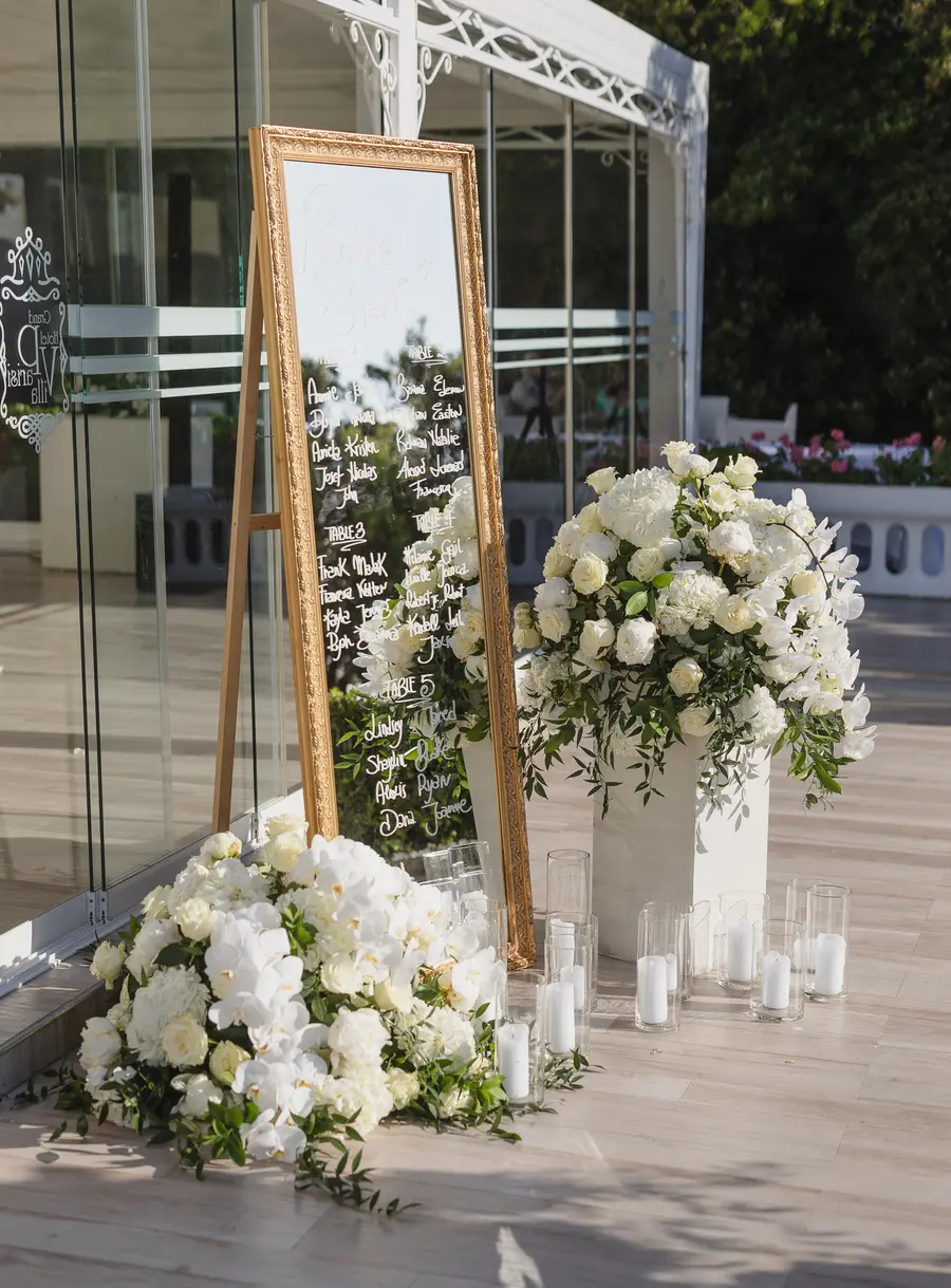 Wedding seating chart on a gold-framed mirror with white flowers and candles