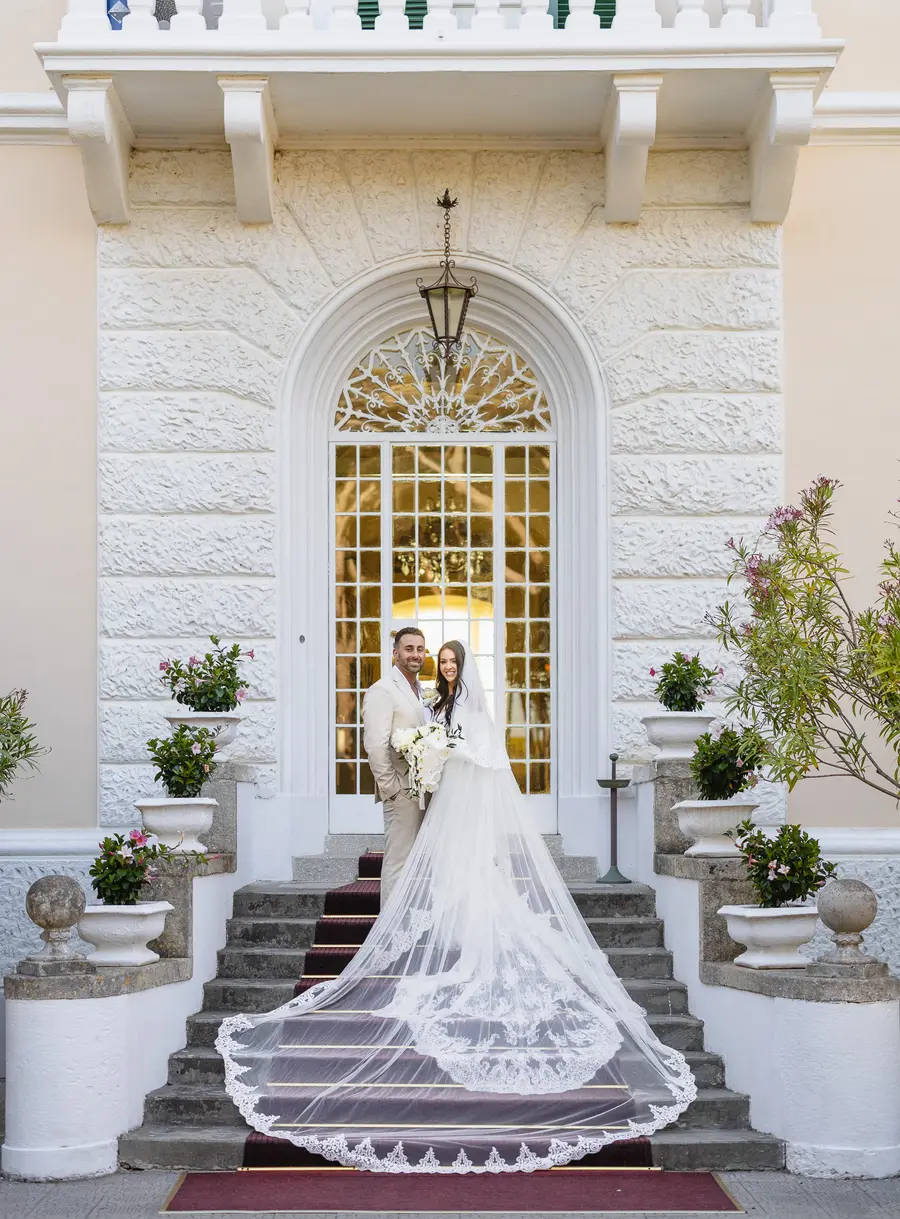 Couple at the top of the Villa Parisi staircase with the long lace veil over the steps