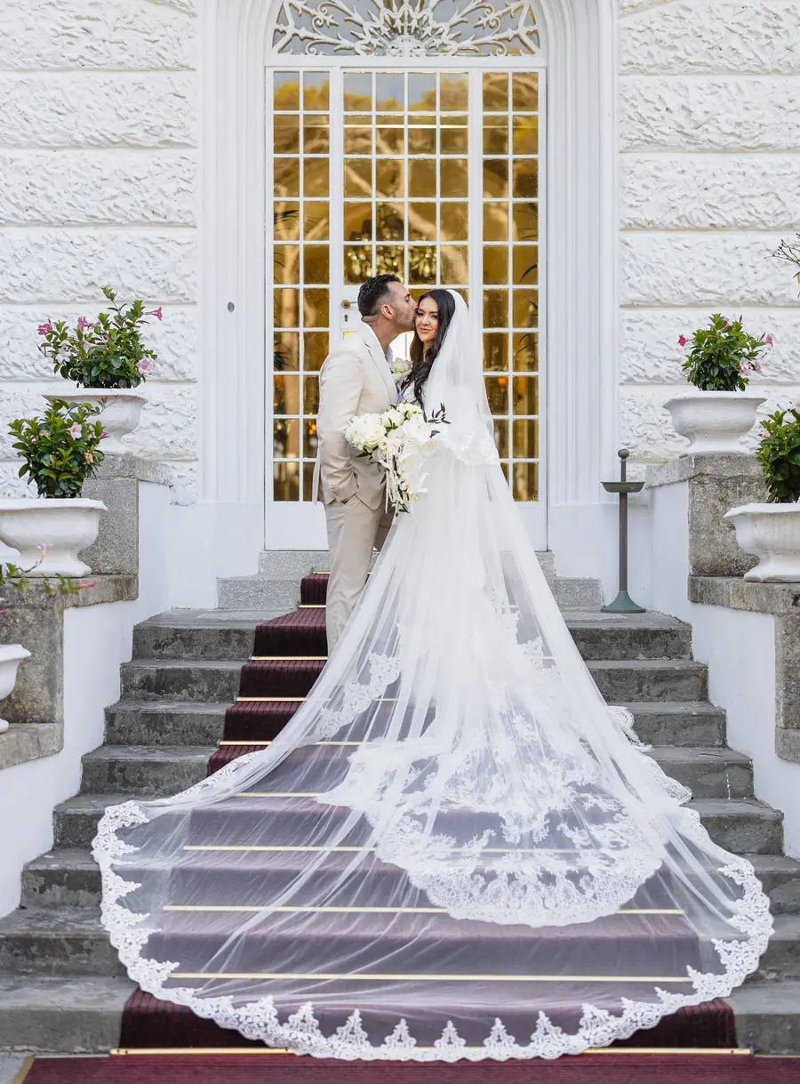 Cheek kiss on the Villa Parisi staircase with the lace veil trailing down the steps