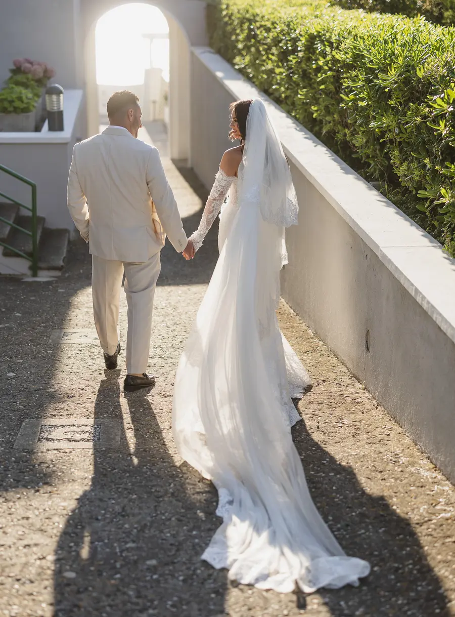 Newlyweds hand in hand in golden backlight along the villa path at sunset