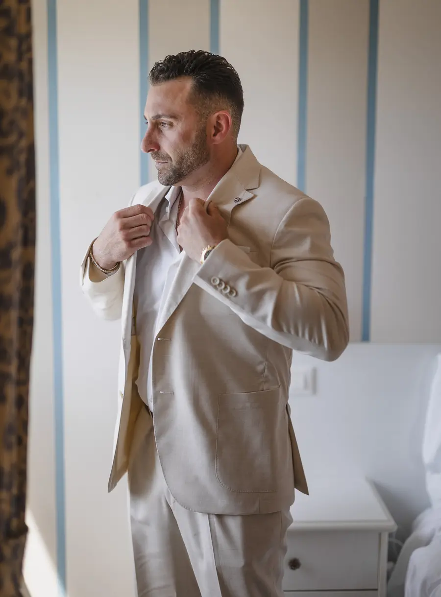 Groom in a beige suit adjusting his jacket during the wedding preparations