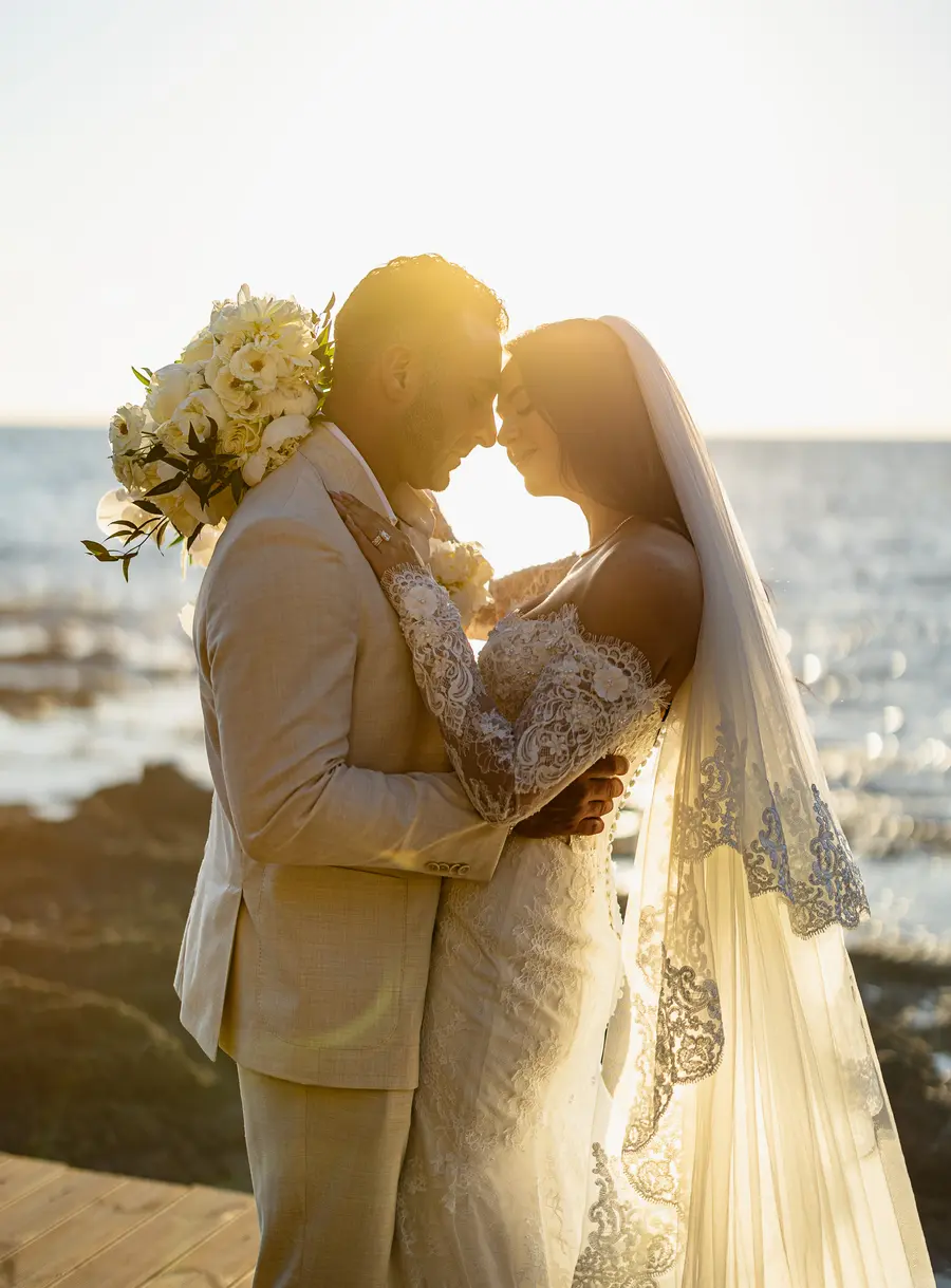 Newlyweds embracing forehead to forehead in golden sunset backlight by the sea