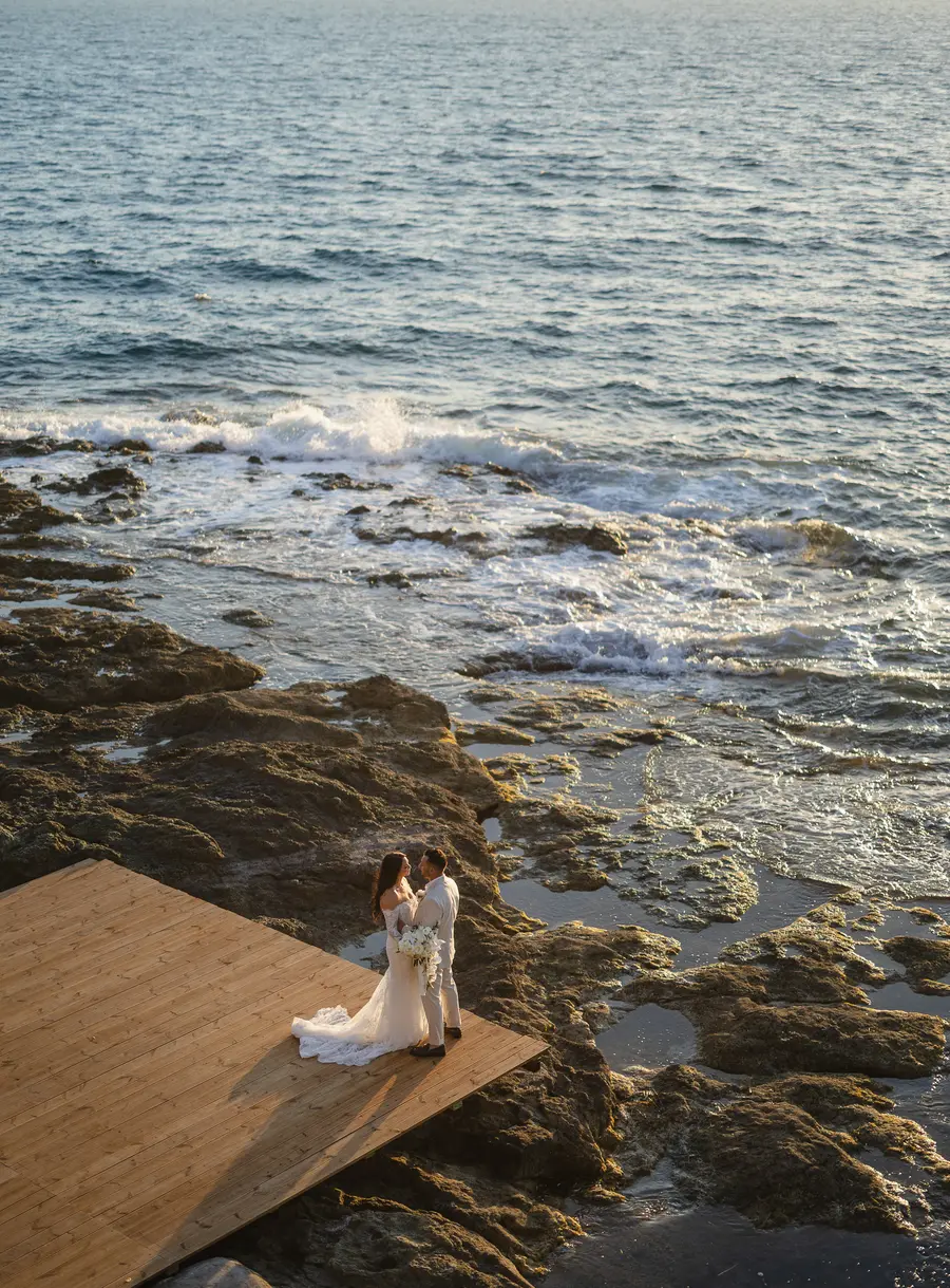 High-angle view of the couple on the wooden deck among rocks and waves in Castiglioncello
