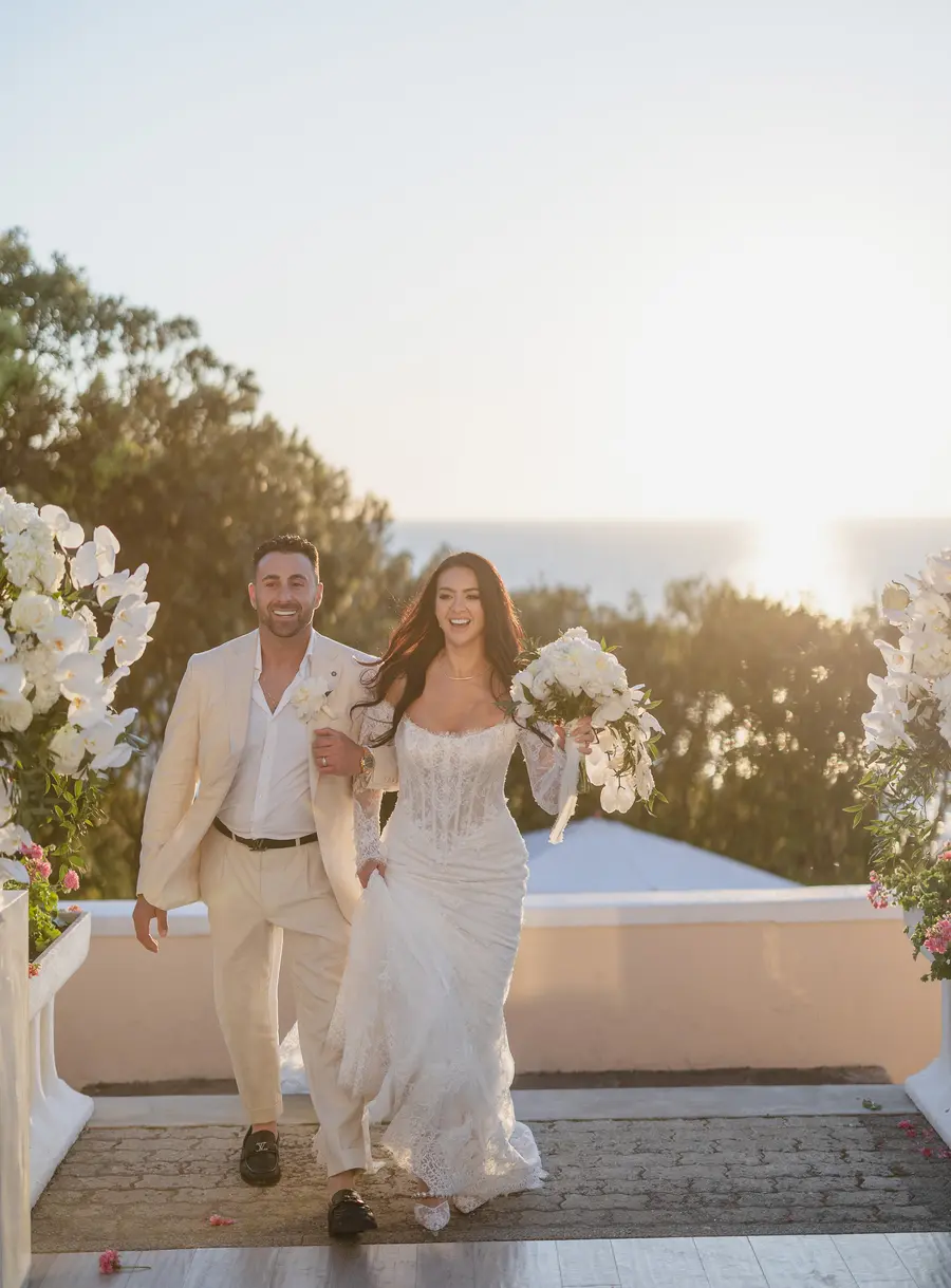 Smiling newlyweds climbing the terrace steps at sunset towards the reception