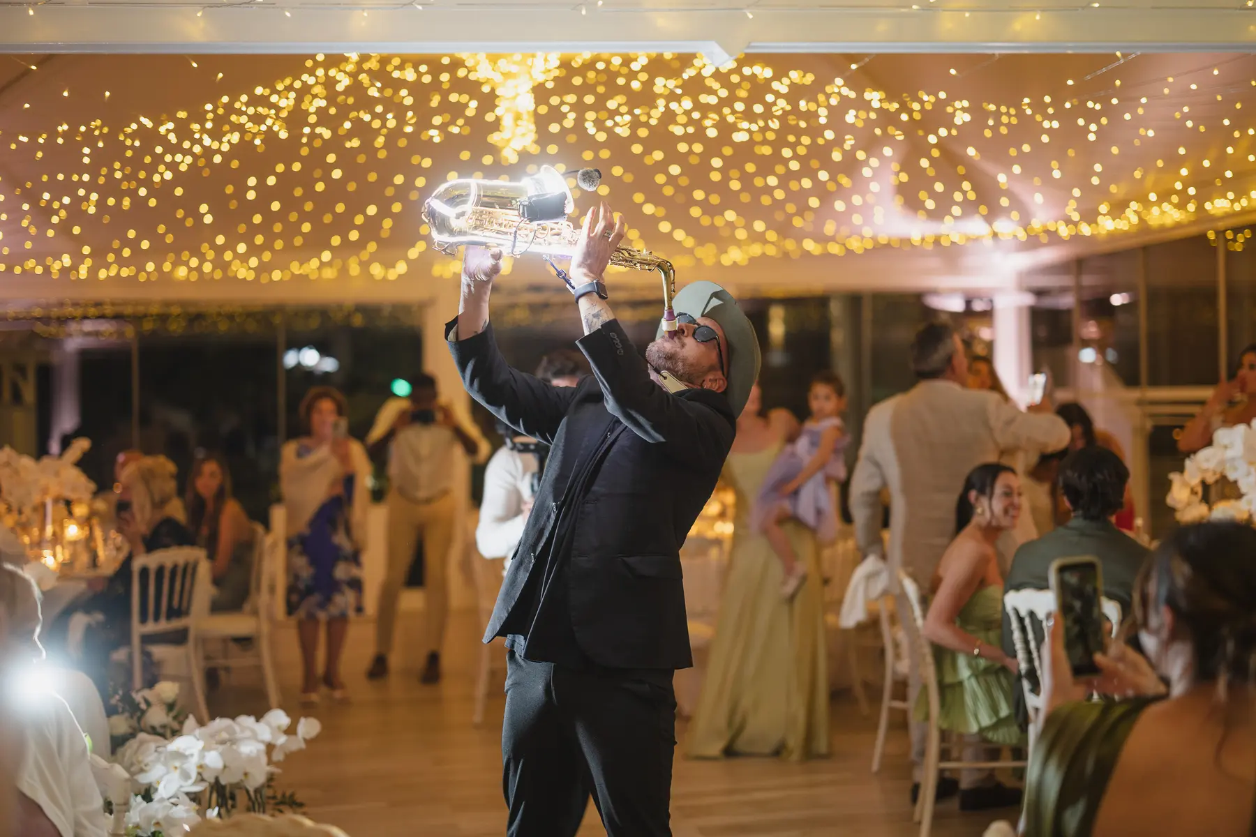 Saxophonist with a glowing sax entertaining guests at the wedding dinner under string lights